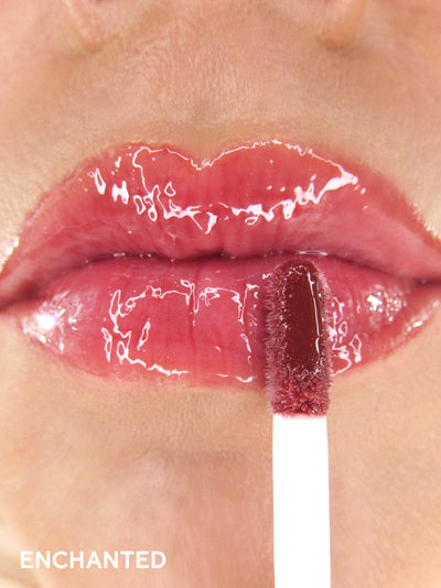 Enchanted -- close up of model applying mauve tinted lip oil to lips