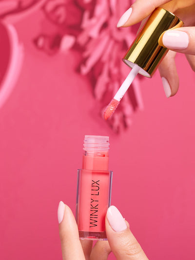Juicy -- model hand pulling pink lip oil out applicator out of component on pink background