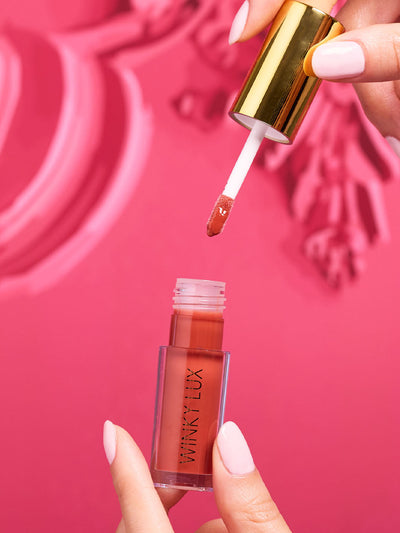 Swoon -- stylized image of model hand taking applicator out of pink tinted lip oil component